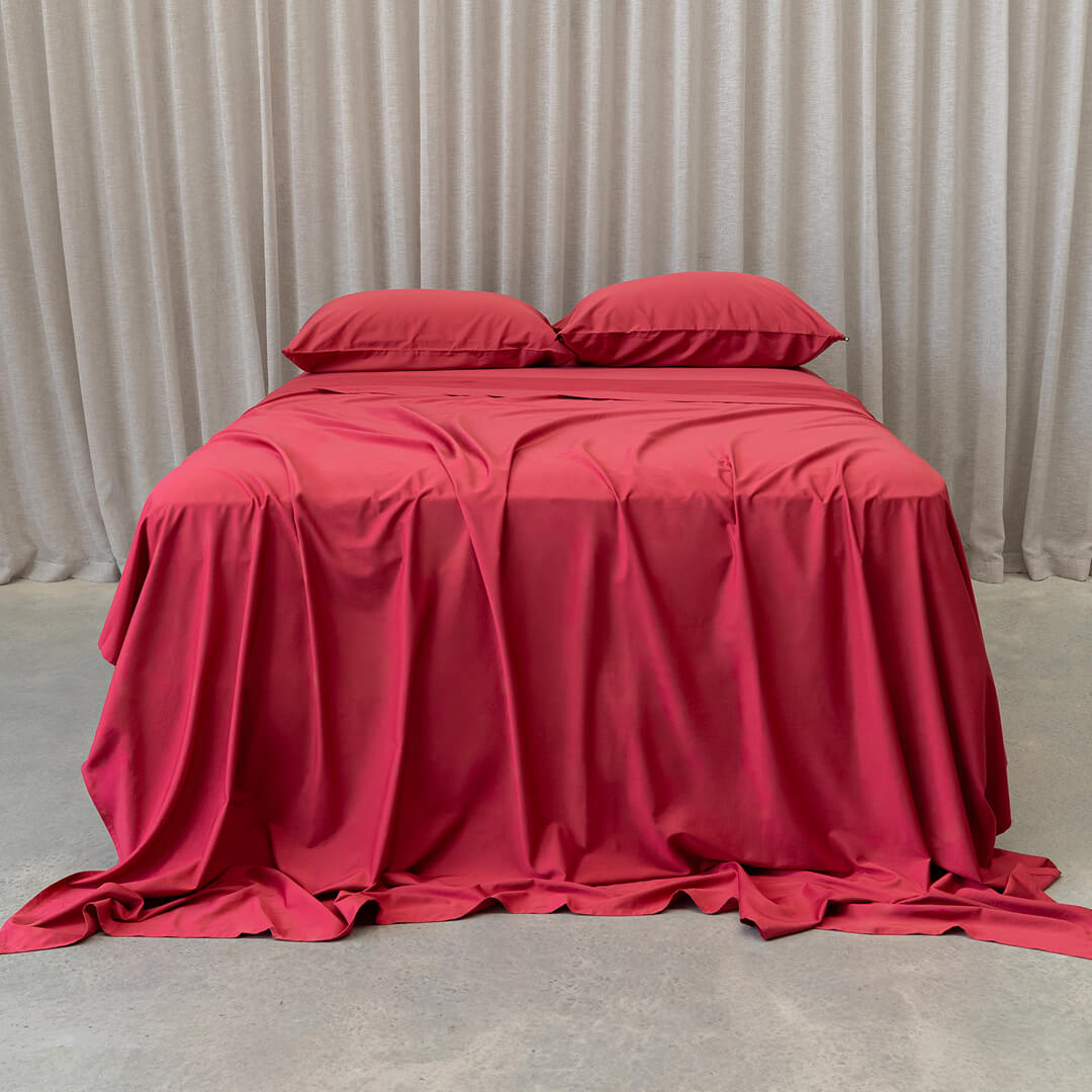 Red bedspread with matching pillows on a bed against a beige curtain background.