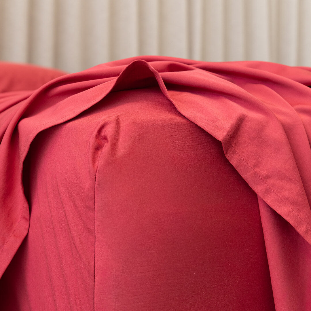 Close-up of red fabric fitted sheet corner on mattress. 