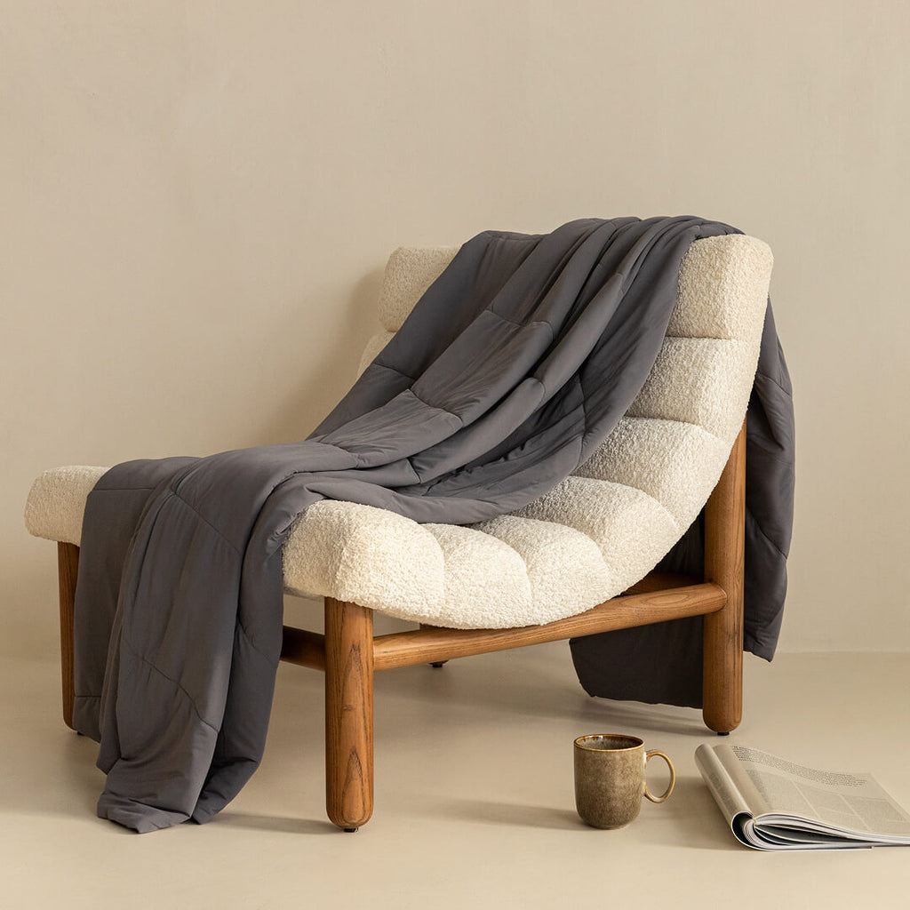 Charcoal coloured cooling blanket draped over a fashionable lounge chair. 