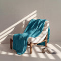 Blue cooling blanket draped over a white chair with a cup and book on a light surface.