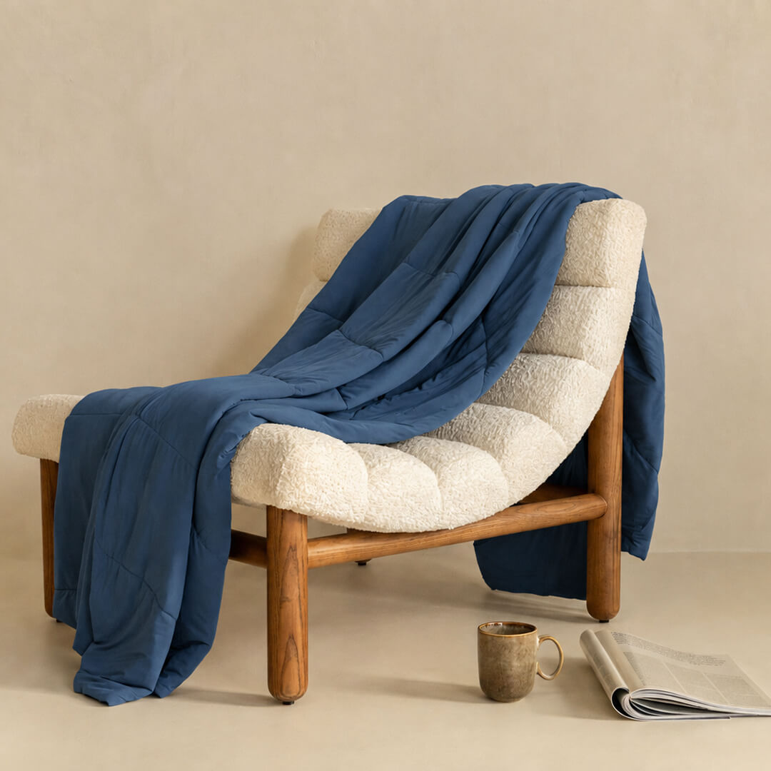 Chair with a blue cooling blanket draped over it, next to a cup and newspaper on a beige surface.