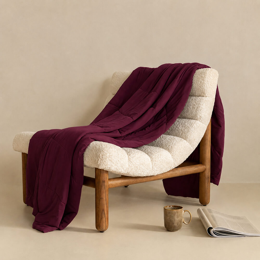 Chair with a burgundy blanket draped over it, next to a cup and magazine on a beige surface.