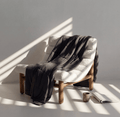 White armchair with a dark cooling grey blanket draped over it, sunlit room.