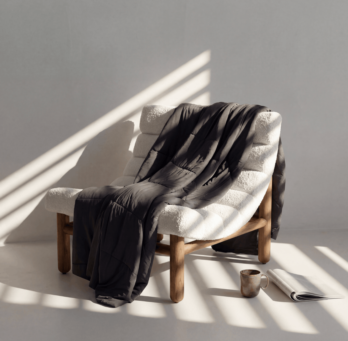 White armchair with a dark cooling grey blanket draped over it, sunlit room.