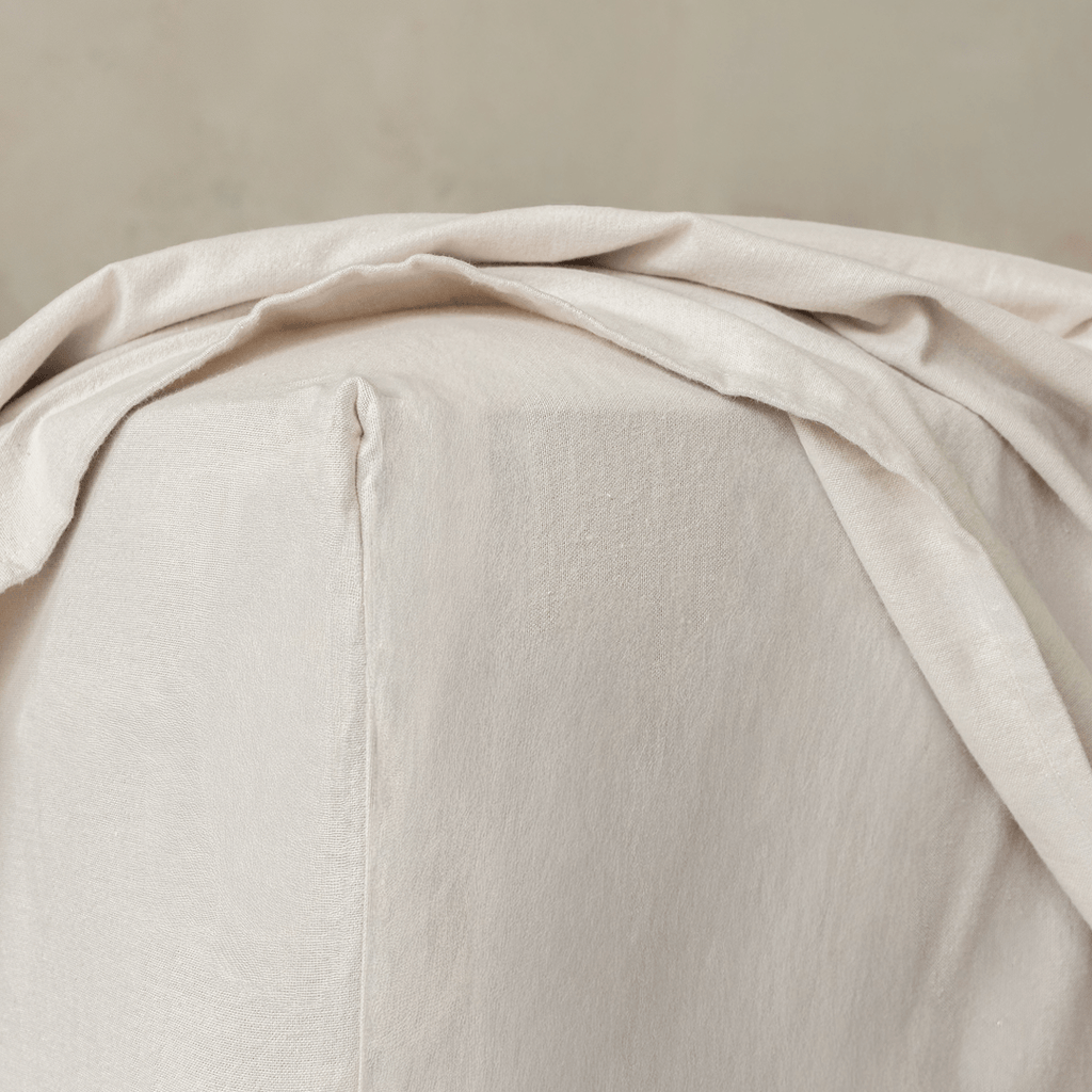 Close-up of a beige fitted sheet corner, highlighting the elasticized edge and tailored construction designed for a secure mattress fit.