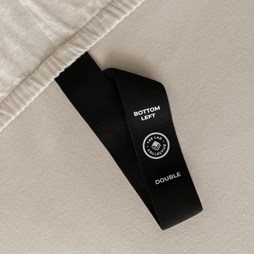 Close-up of a fitted sheet orientation tag labeled “Bottom Left” against beige fabric, designed to simplify bed-making and identify the correct sheet position.