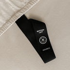 Close-up of a fitted sheet orientation tag labeled “Bottom Left” against beige fabric, designed to simplify bed-making and identify the correct sheet position.