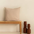 Beige European waffle pillow on a wooden bench with two brown vases against a beige wall.