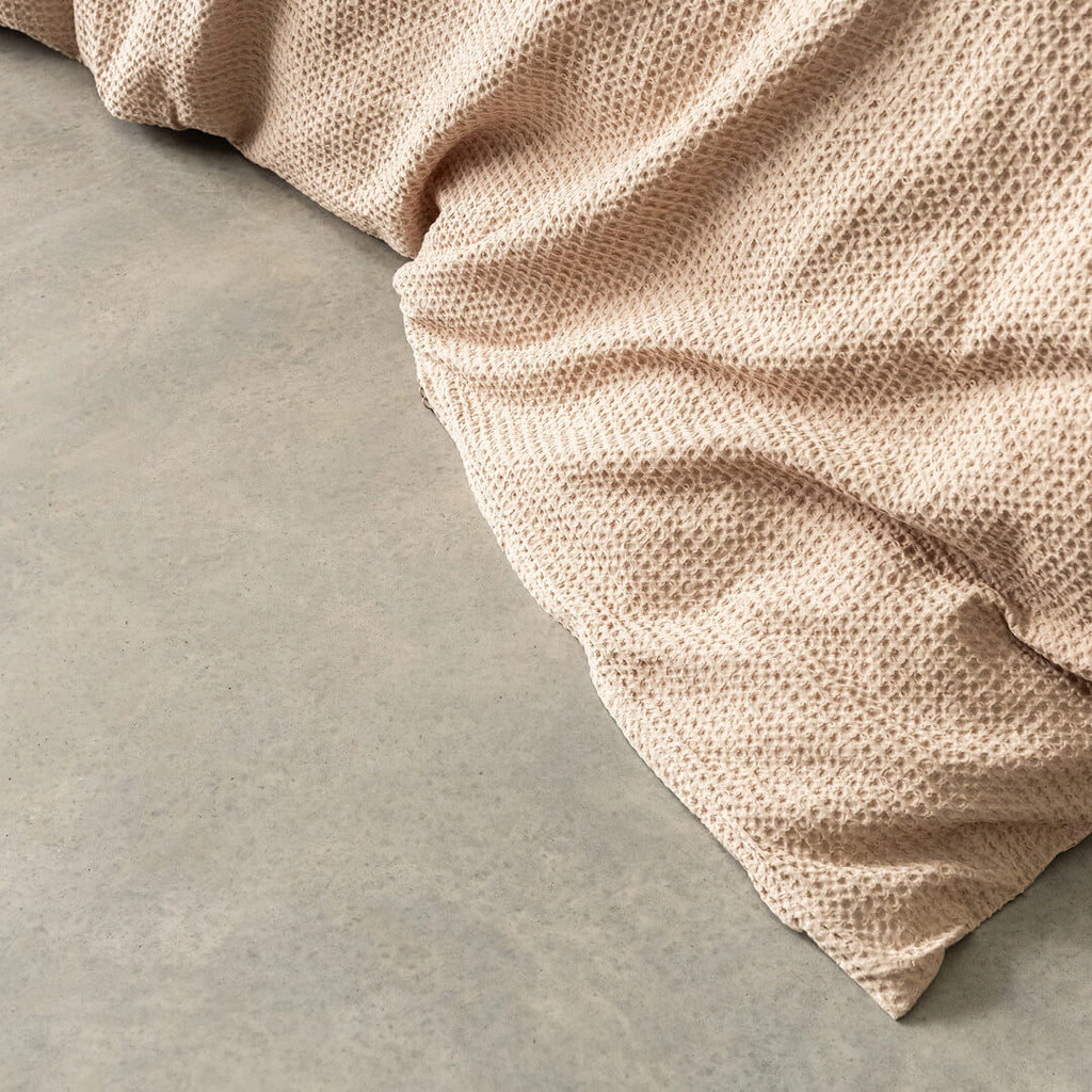 Close-up of a textured beige quilt cover corner on a grey concrete surface.