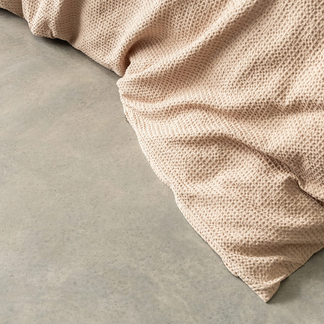Close-up of a textured beige quilt cover corner on a grey concrete surface.