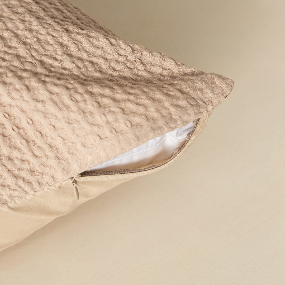 Textured beige pillow with a zipper on a beige background.