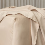 Beige bed sheets draped over a bed with a neutral background.