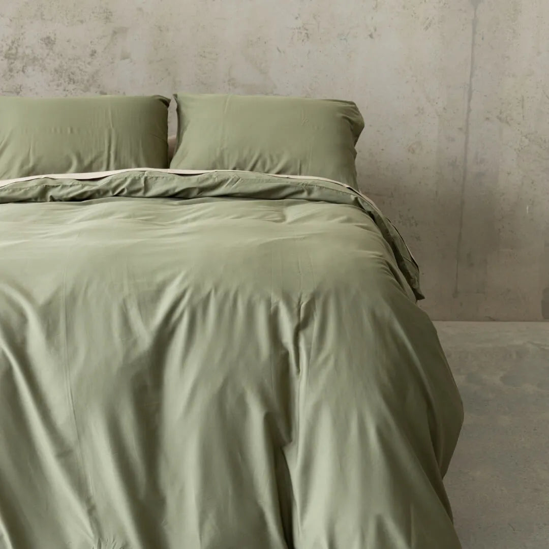 Sage green quilt cover set on a bed, against a neutral concrete look backdrop.