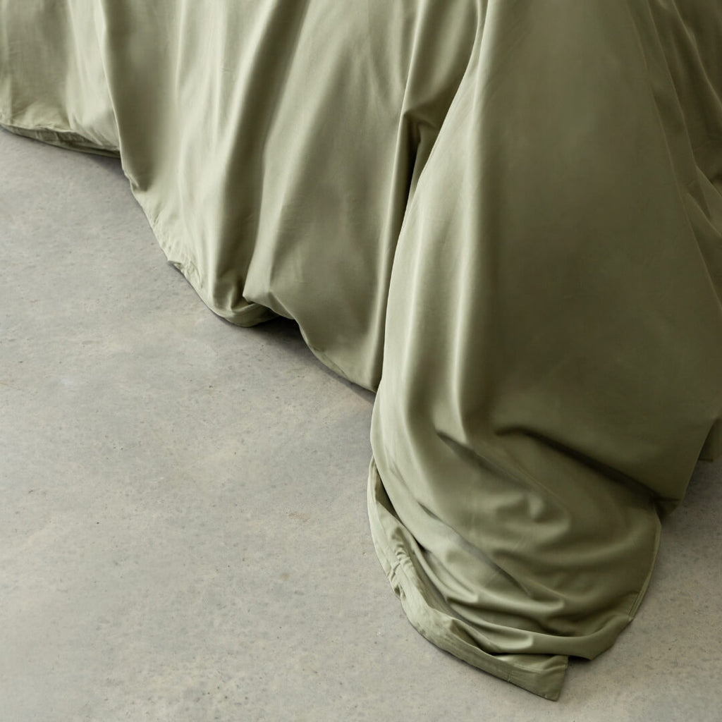 Sage green quilt cover magnetic close-up, draped over bed.