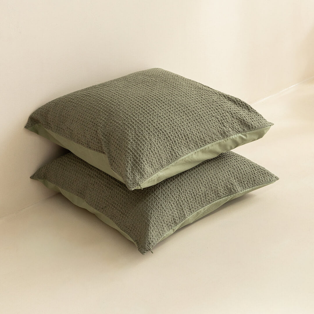 Two green textured European pillows on a beige surface.