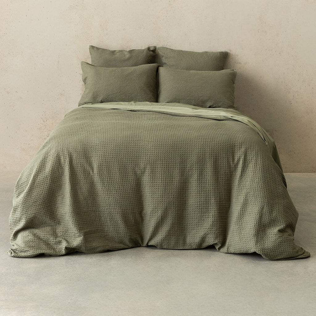 Green textured bedding set on a bed against a beige wall.