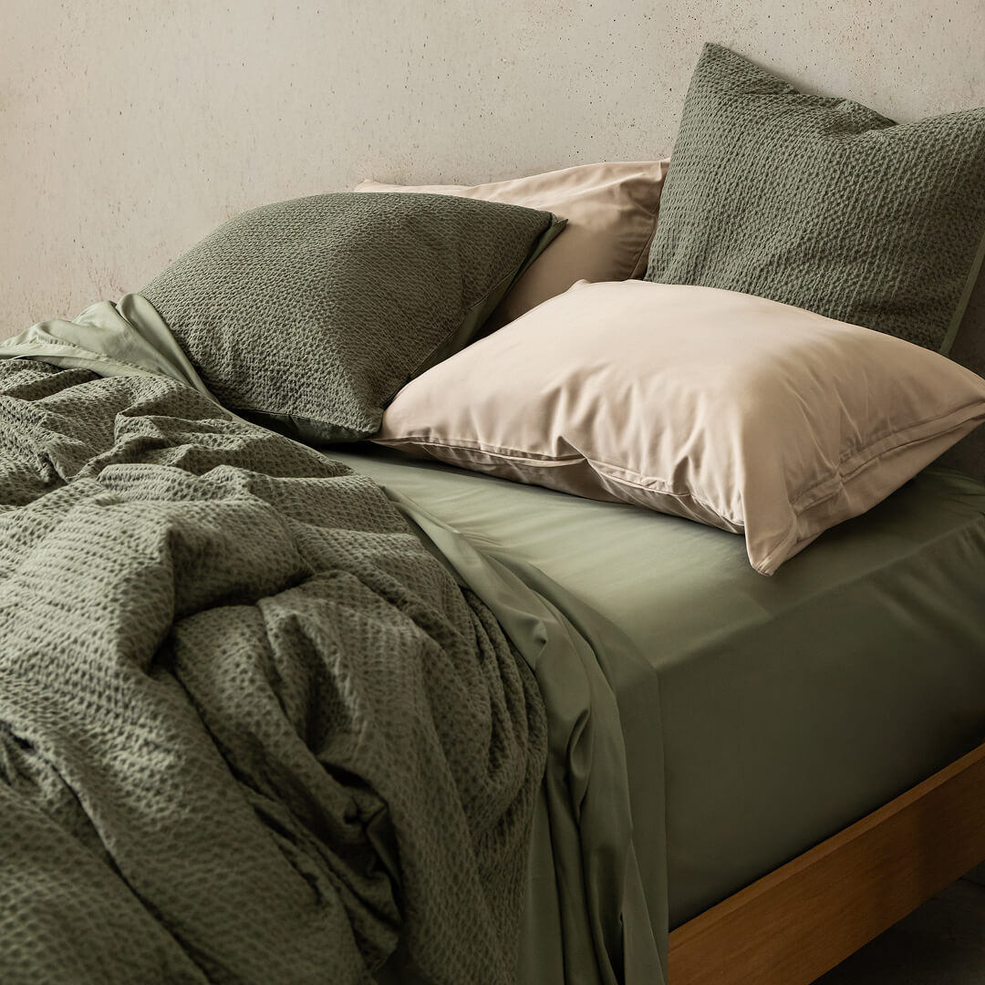 Bed with green bedding and pillows against a neutral wall.