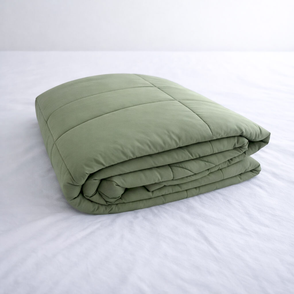 Folded green cooling blanket on a white bed.