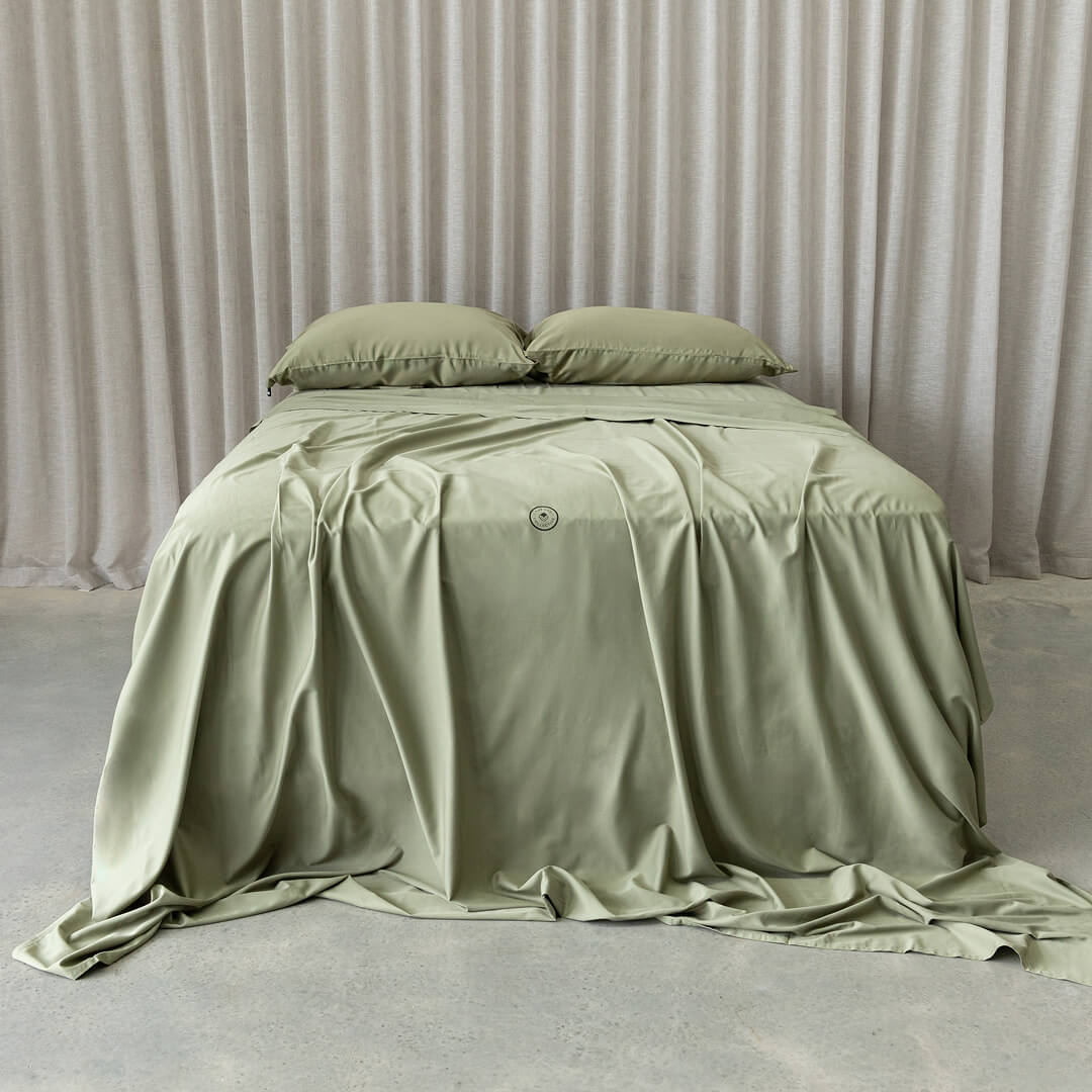 Green bedspread on a bed with matching pillows against a neutral background.