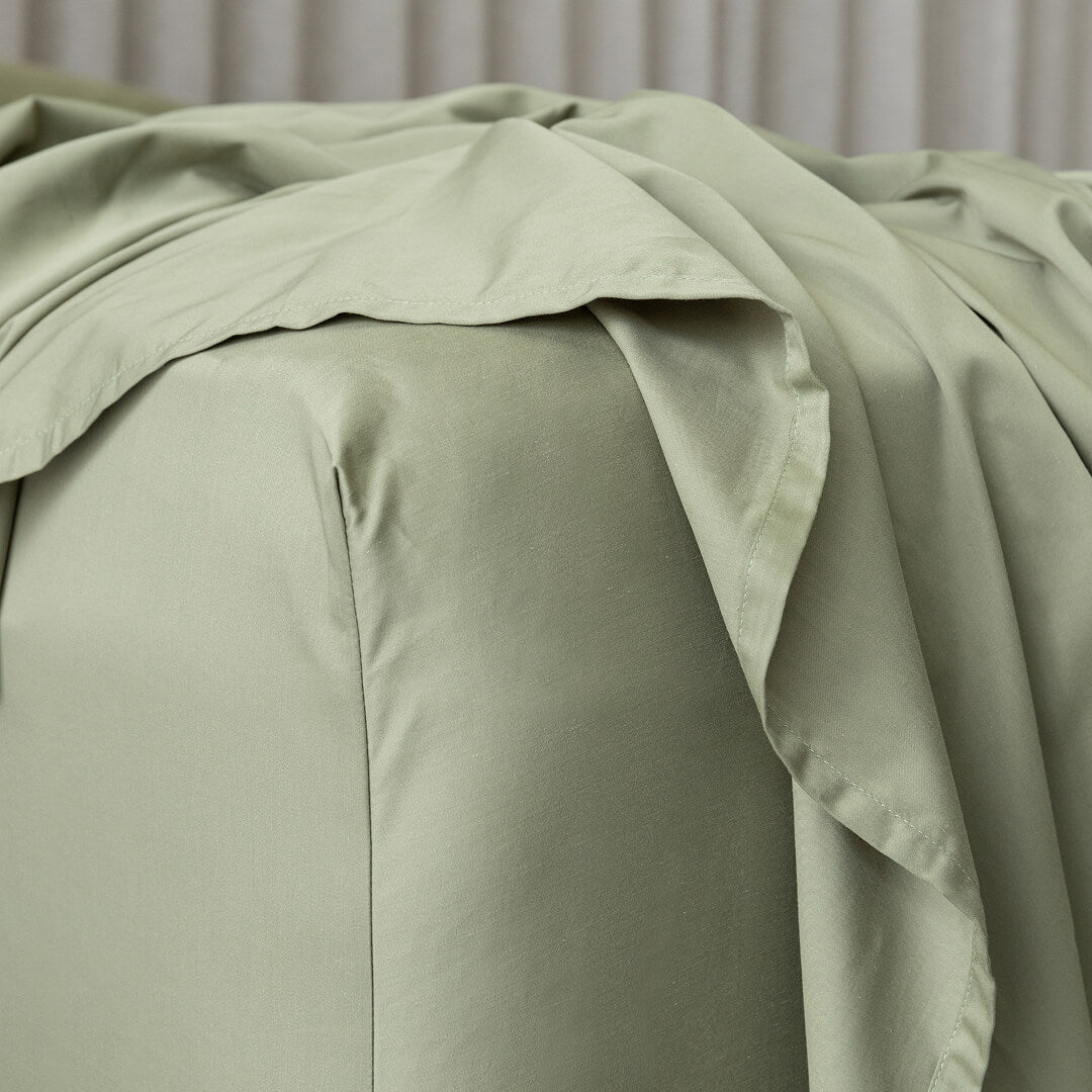 Green bed sheets on a bed with a neutral background.