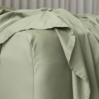 Green bed sheets on a bed with a neutral background.