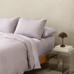 Angled view of the Daylesford lilac quilt cover set with matching pillowcases on a modern bed.
