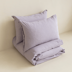 Angled view of the folded Daylesford lilac quilt cover set with matching pillowcases.