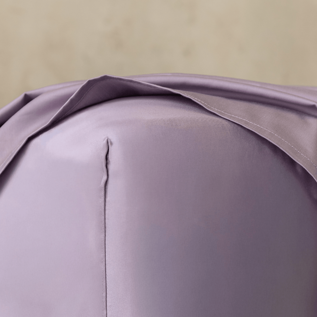 Close-up of a lavender fitted sheet stretched over the corner of a mattress, showing the smooth fabric, stitched seam, and snug fit.