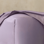 Close-up of a lavender fitted sheet stretched over the corner of a mattress, showing the smooth fabric, stitched seam, and snug fit.