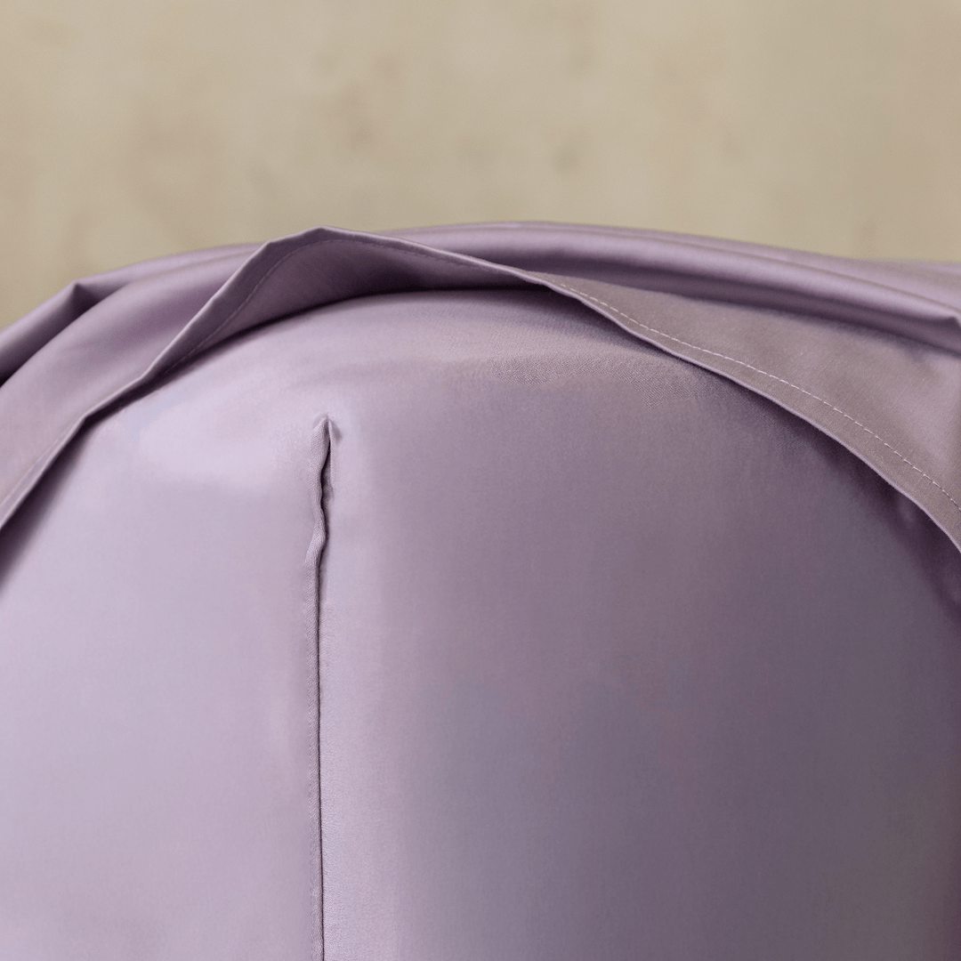 Close-up of a lavender fitted sheet stretched over the corner of a mattress, showing the smooth fabric, stitched seam, and snug fit.