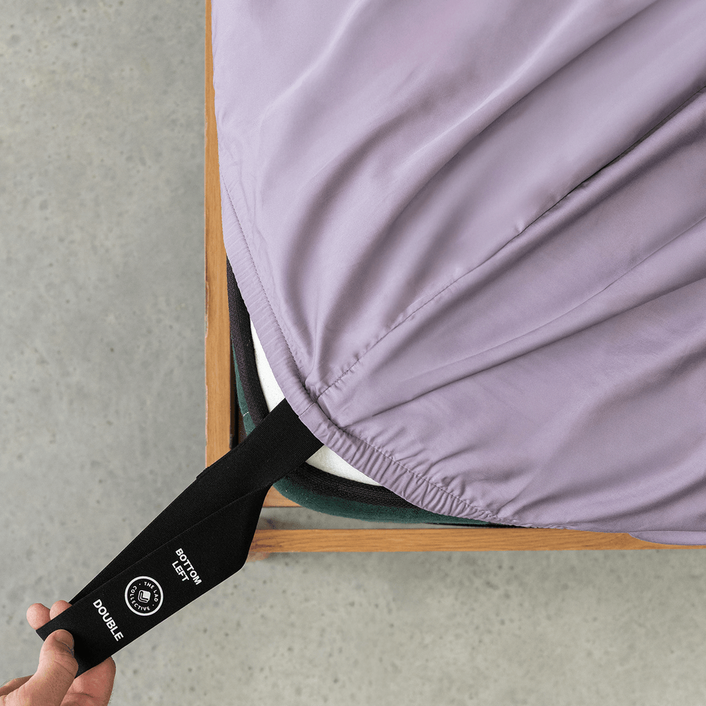 Daylesford fitted sheet secured over a mattress with the labeled corner strap pulled into view, demonstrating the easy-fit design.