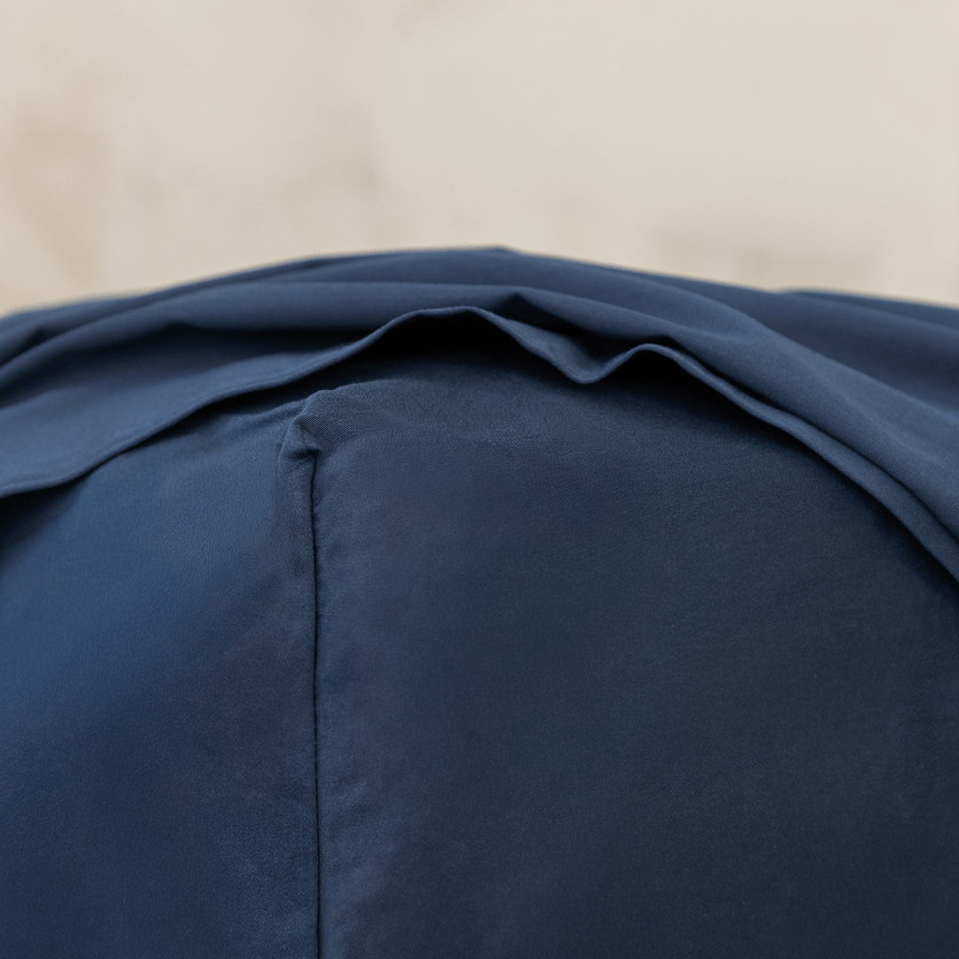 Close-up corner detail of a navy blue fitted sheet and top flat sheet showing smooth fabric texture and seam stitching