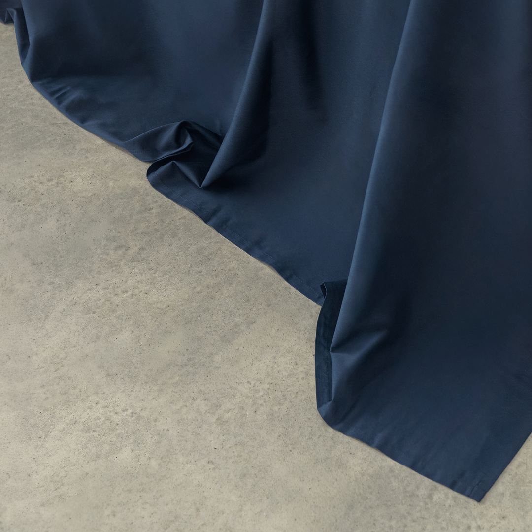Close-up of navy blue sheet fabric cascading smoothly onto a light gray concrete floor