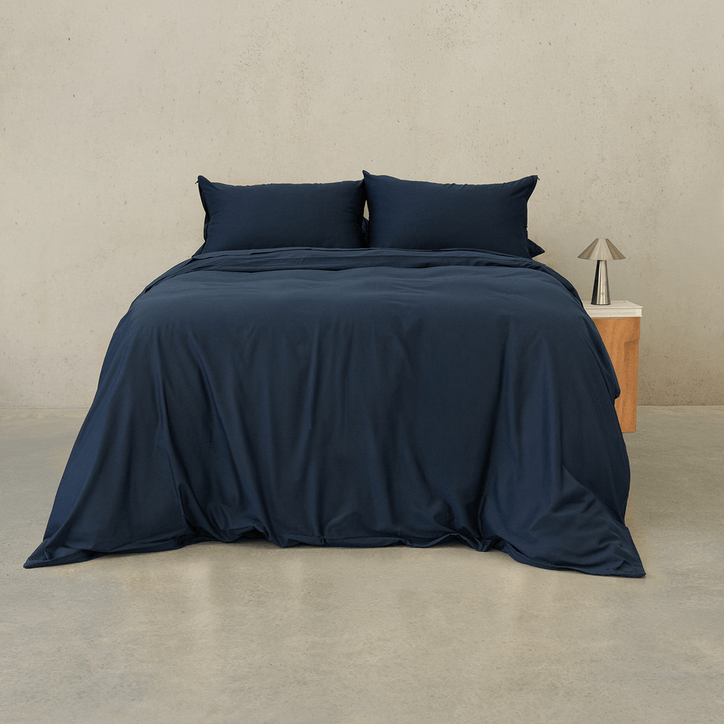 Navy blue quilt cover set made up on a double bed with two matching pillowcases against a neutral wall