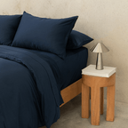 Side view of a double bed styled with a navy blue quilt cover, matching pillowcases, and a modern bedside lamp