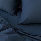 Close-up angle view of two navy blue pillowcases and a folded flat sheet on a bed