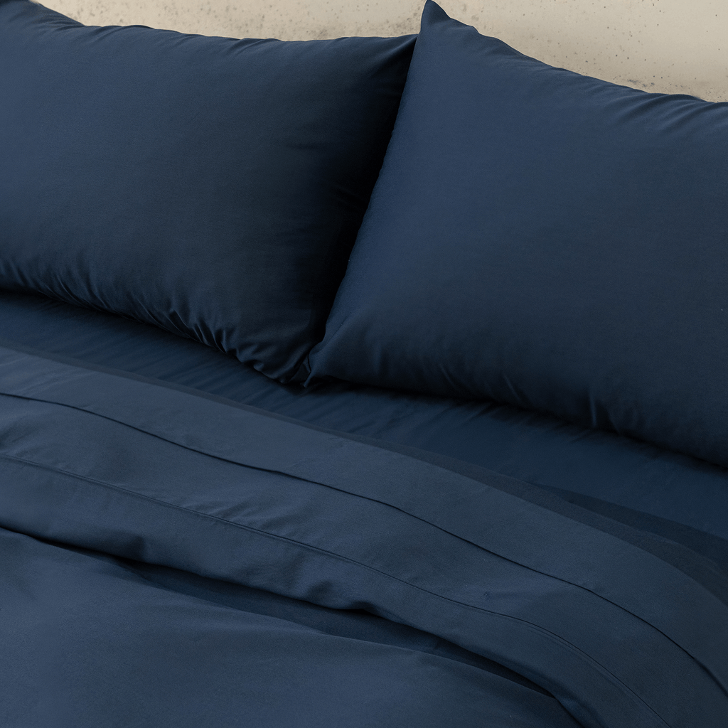 Close-up view of navy blue pillowcases resting above a matching flat sheet and quilt cover