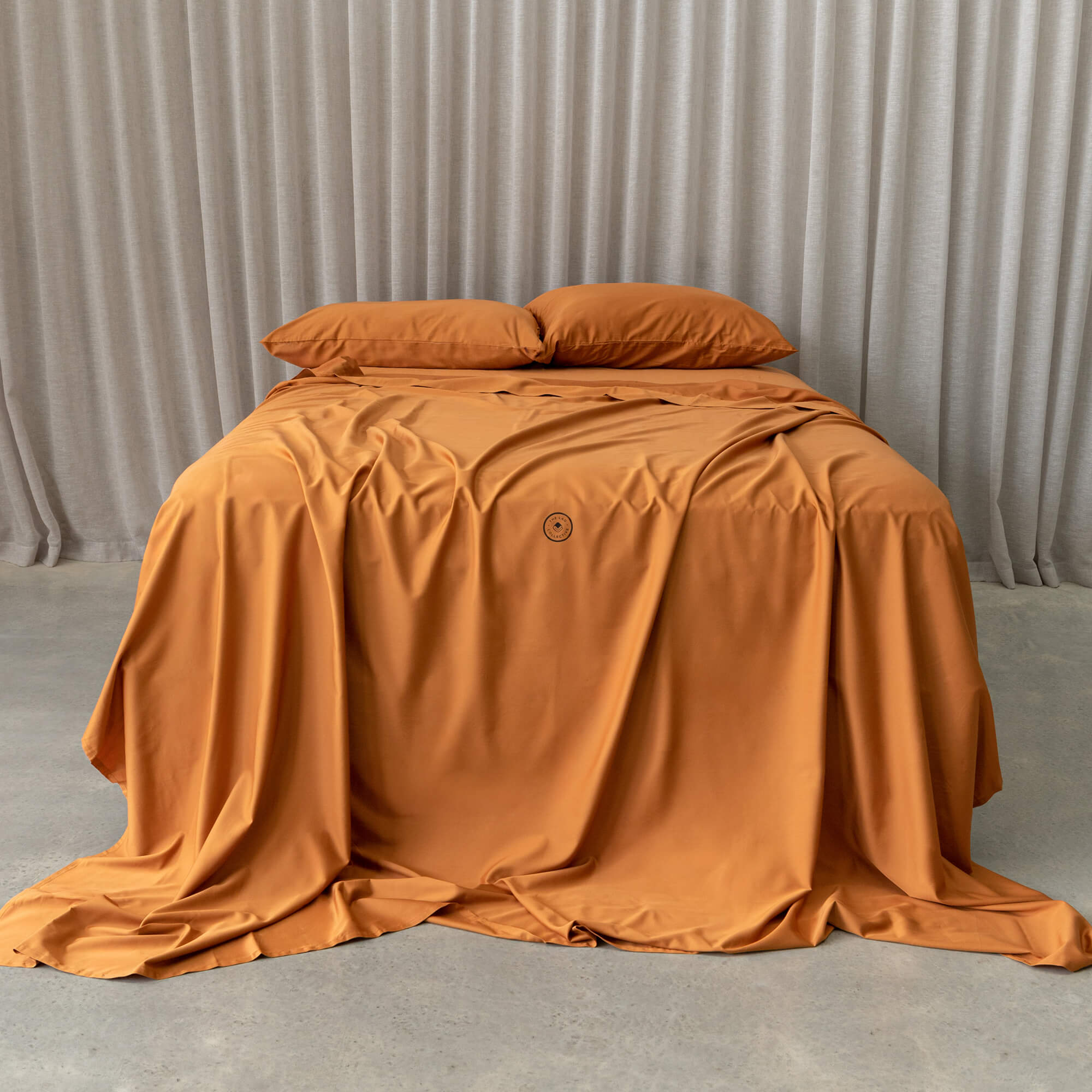Burnt orange bedding set on a bed, against a neutral backdrop and a beige curtain.