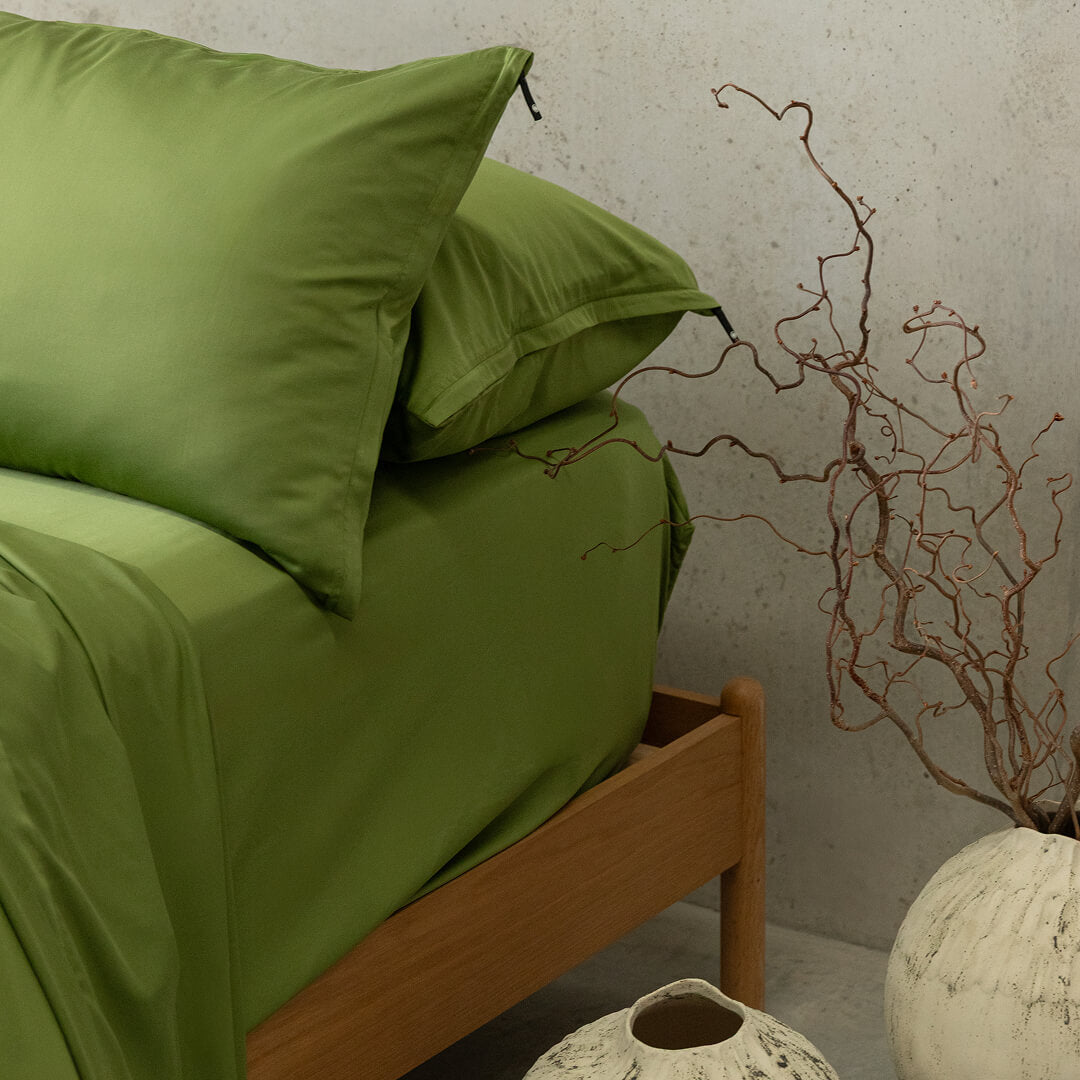 Green bedding set on a bed with decorative branches and vases in the background.