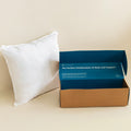 White pillow next to a blue and brown box on a beige background.