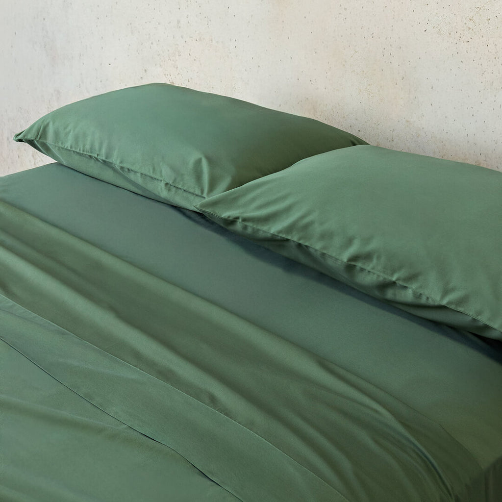 Green bed sheets and pillows on a bed against a neutral wall.