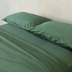 Green bed sheets and pillows on a bed against a neutral wall.