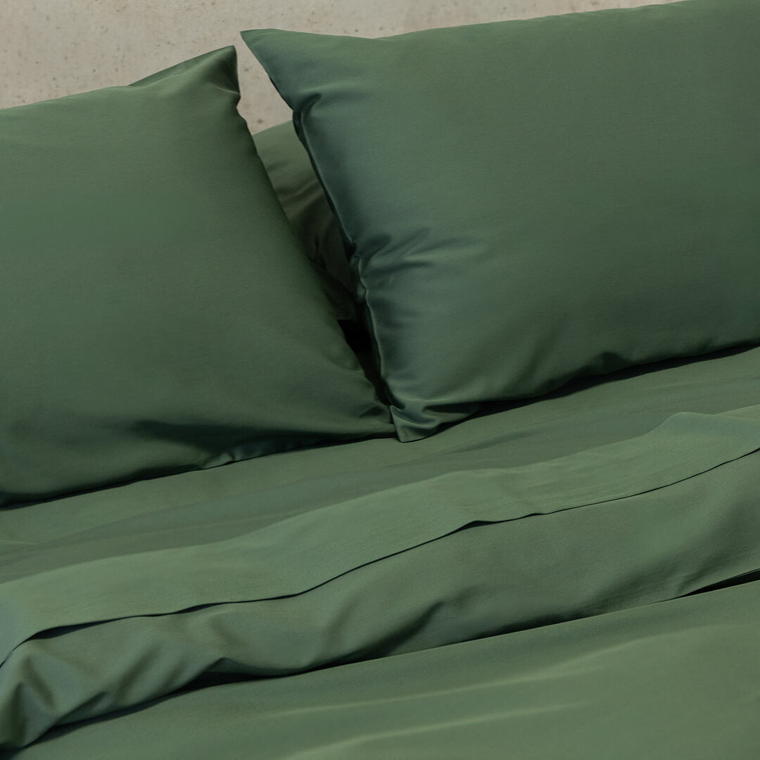 Green bed sheets and pillows on a bed with a neutral background.