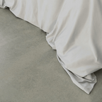Close-up of a soft gray quilt cover draping onto a concrete floor, highlighting its smooth finish and flowing folds.