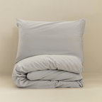 A gray pillow displayed above a neatly folded matching quilt cover against a warm neutral background.