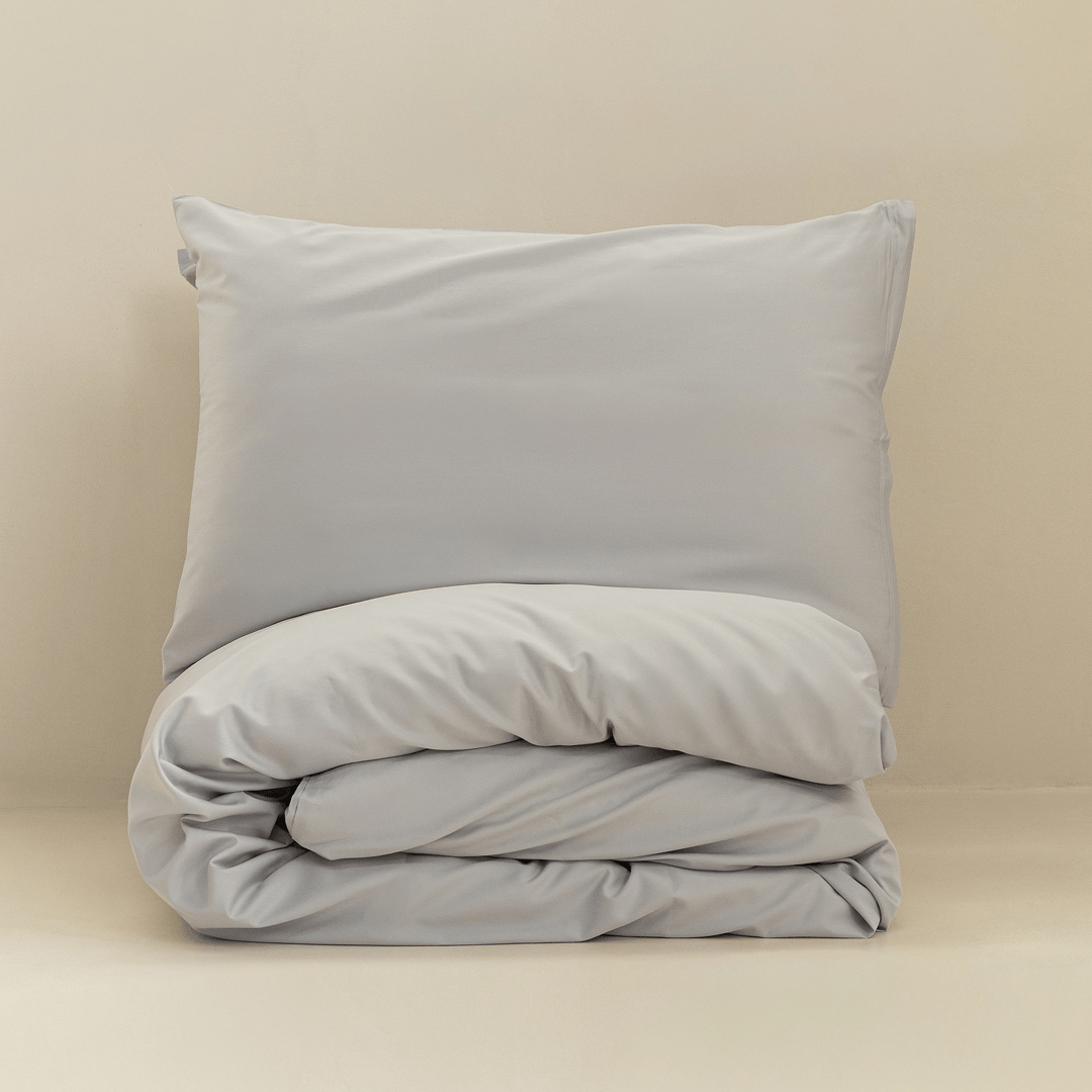 A gray pillow displayed above a neatly folded matching quilt cover against a warm neutral background.