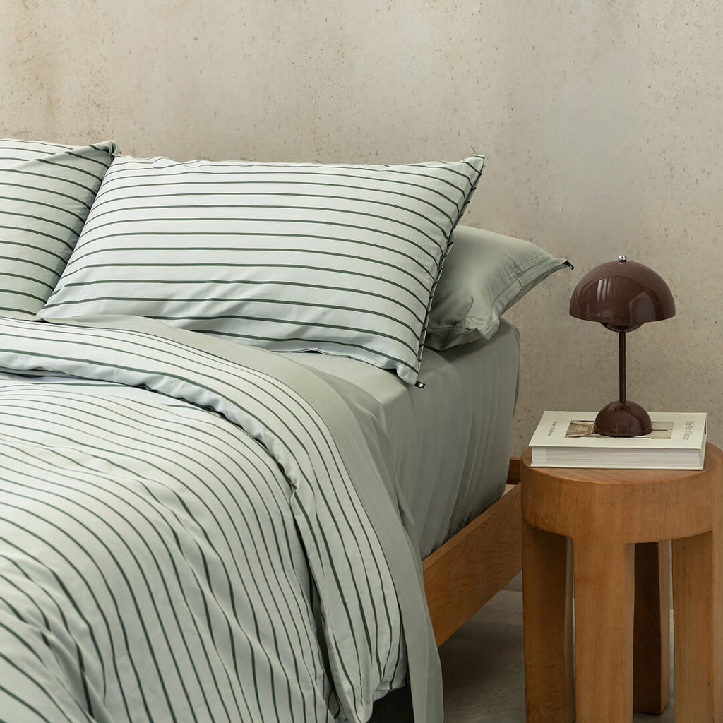 Stripe quilt cover on bed with bedside table, book and lamp.
