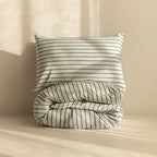 Stripe quilt cover a rolled up on neutral backdrop with pillow on top.