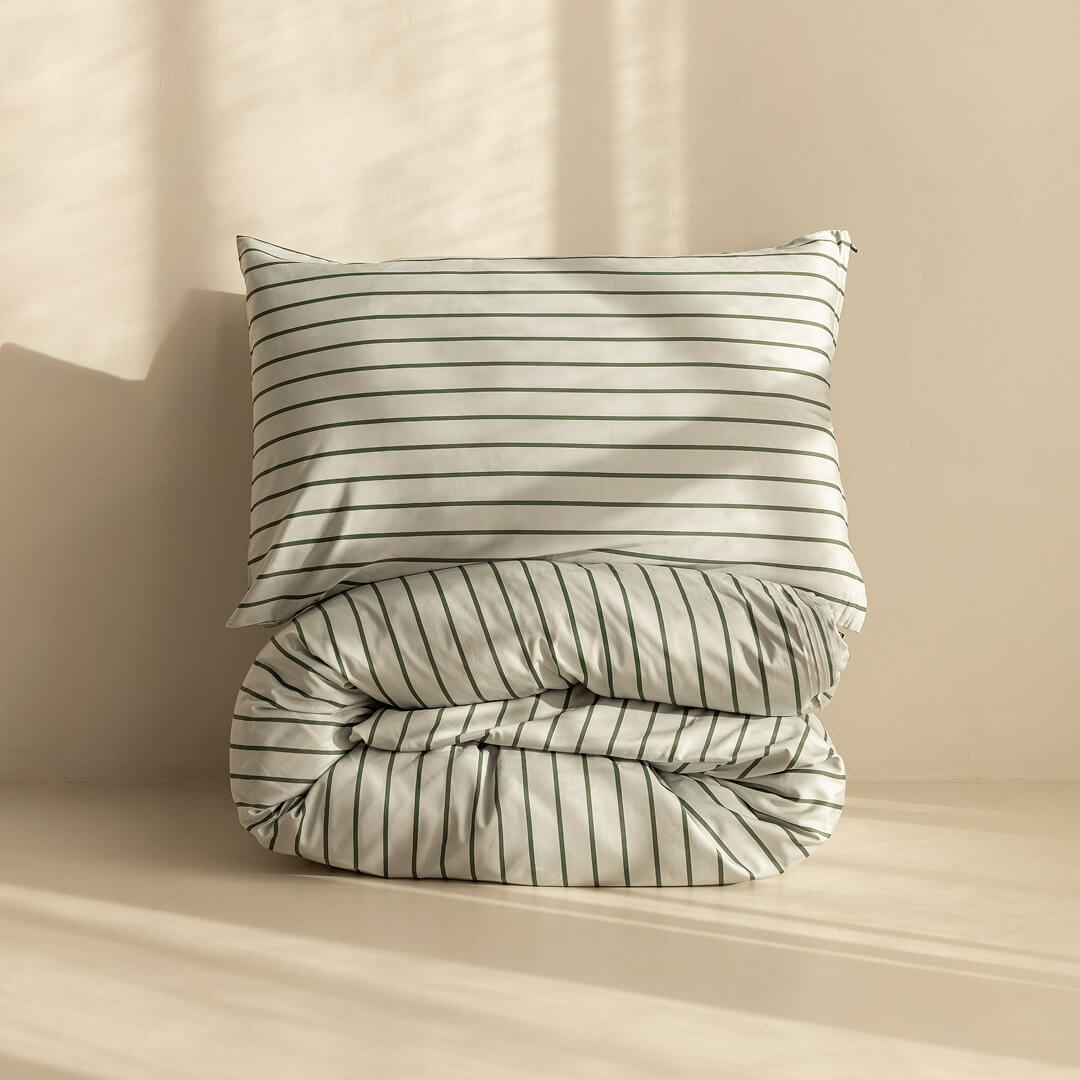 Stripe quilt cover a rolled up on neutral backdrop with pillow on top.