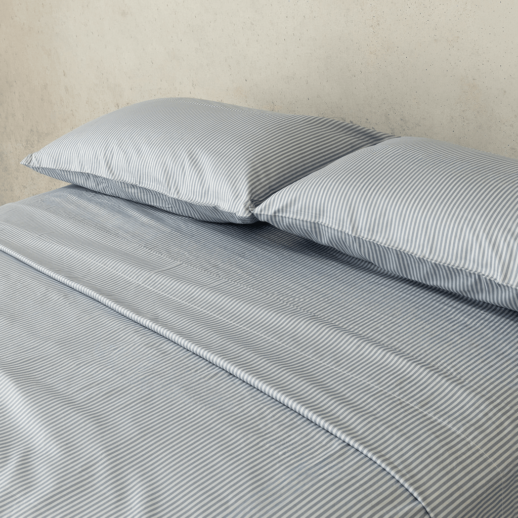 Close-up of two gray and white striped pillows resting on matching striped sheets, highlighting the fine vertical pattern and smooth finish.